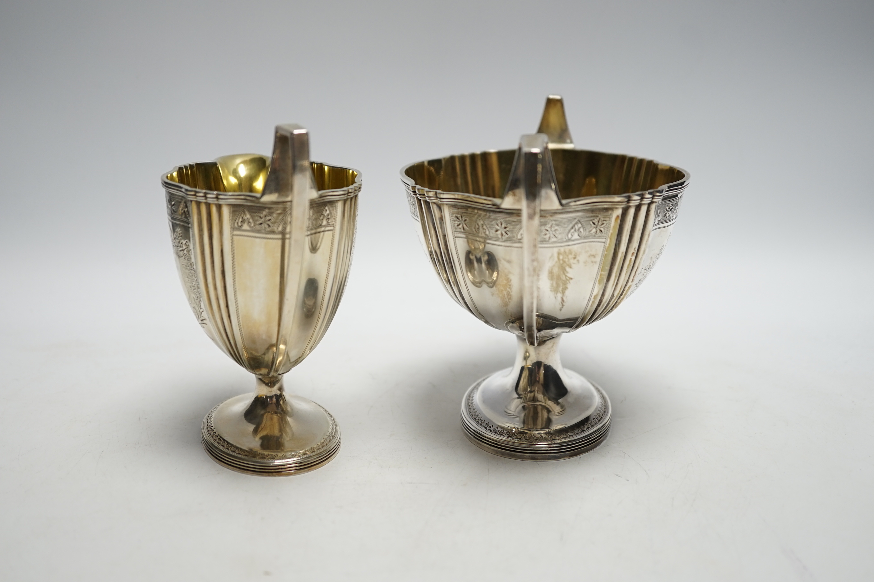 A George III engraved silver two handled oval pedestal sugar bowl and matching cream jug, Henry Chawner, London, 1792, bowl 21.2cm over handles, 20.1oz.